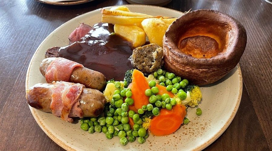 British Sunday roast plate with gravy, sausages, vegetables, and Yorkshire pudding
